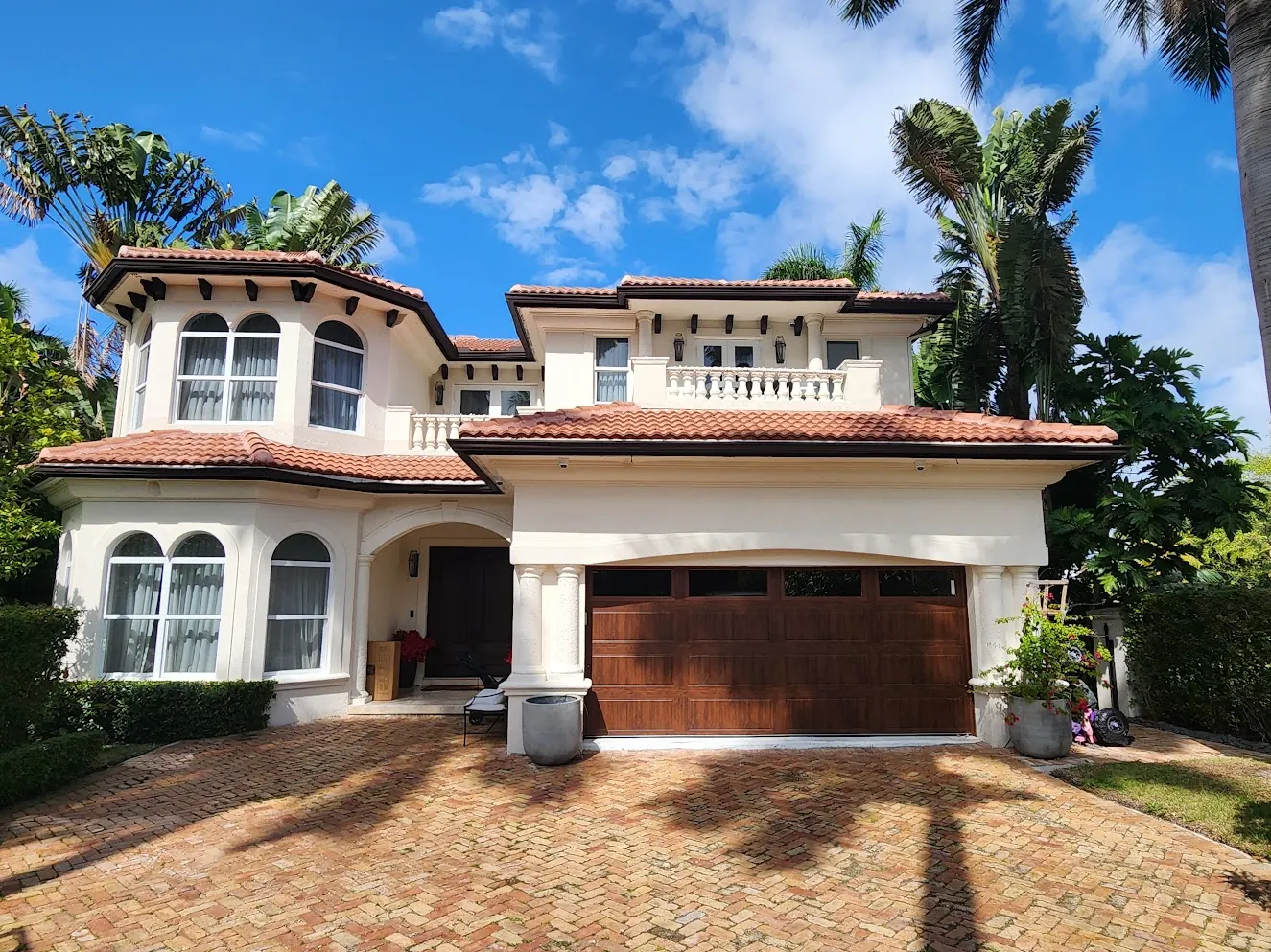 Mediterranean-style home with a wood garage door and paver driveway after an exterior repaint