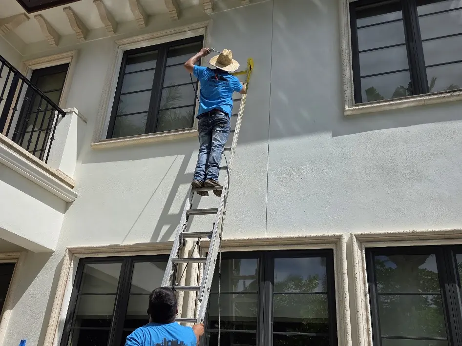 Paint2Last crew on a ladder preparing window trim on a two-story stucco home