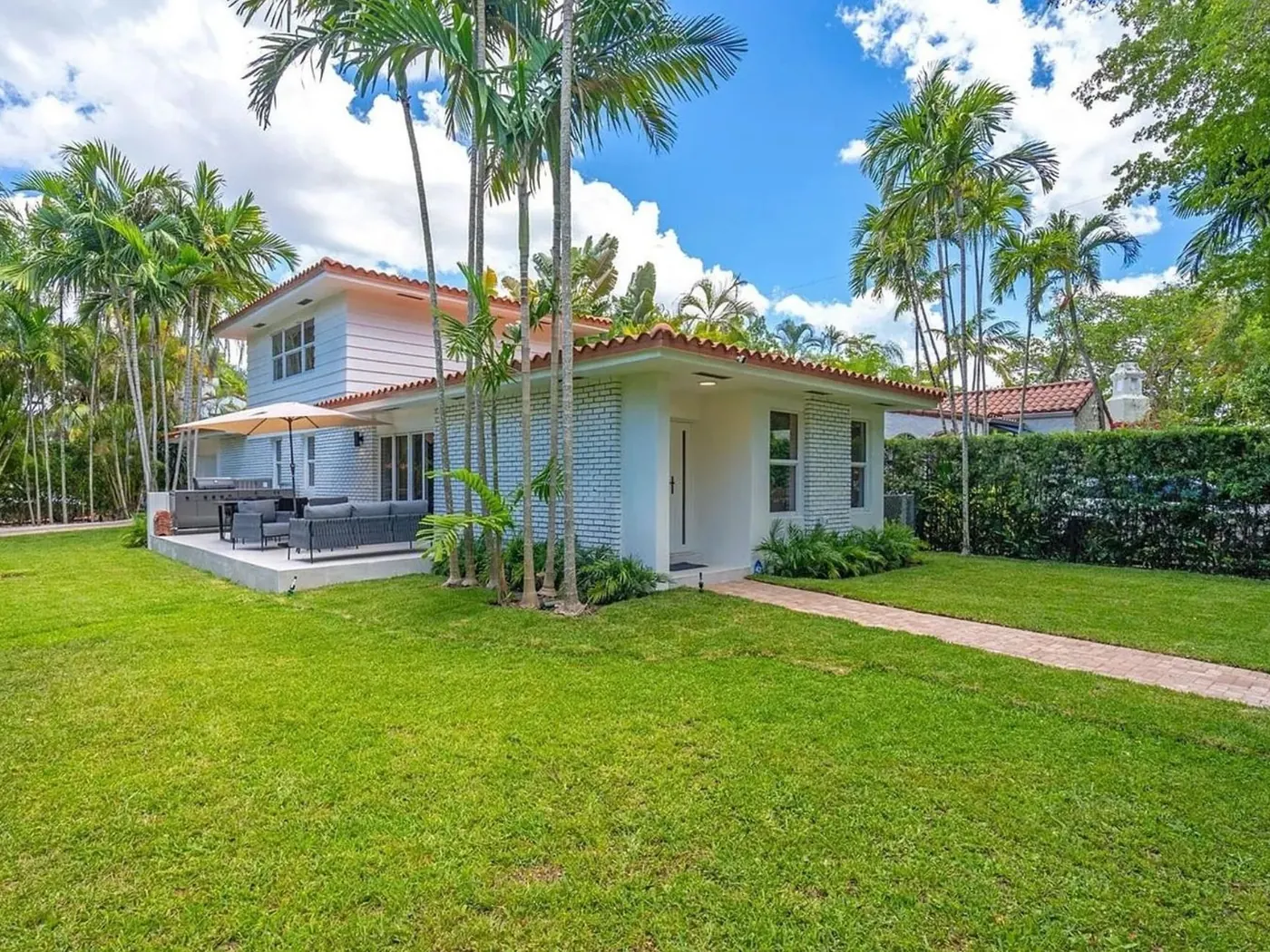 Two-story white home with a barrel-tile roof among palms after an exterior repaint