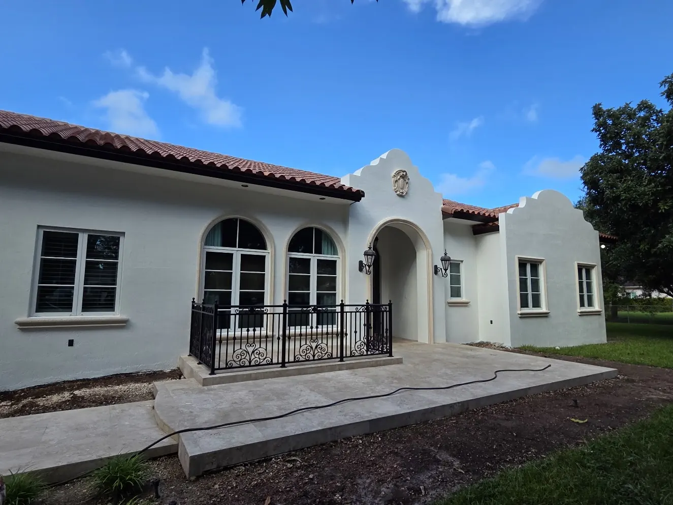 White Spanish Revival home with arched windows and iron railing after an exterior repaint