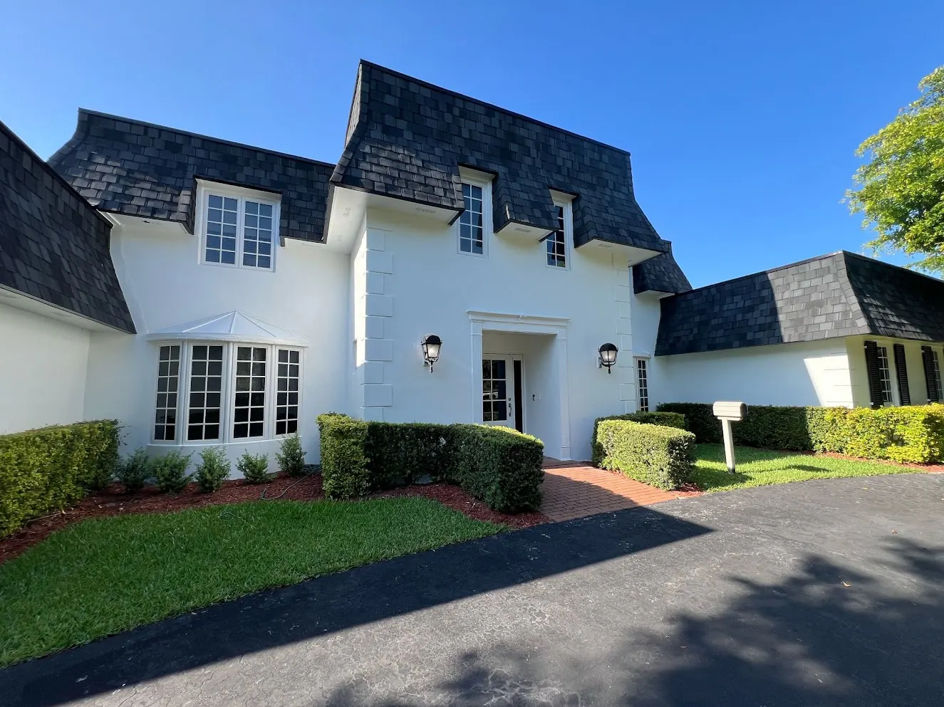 White two-story home with a slate mansard roof after an exterior repaint