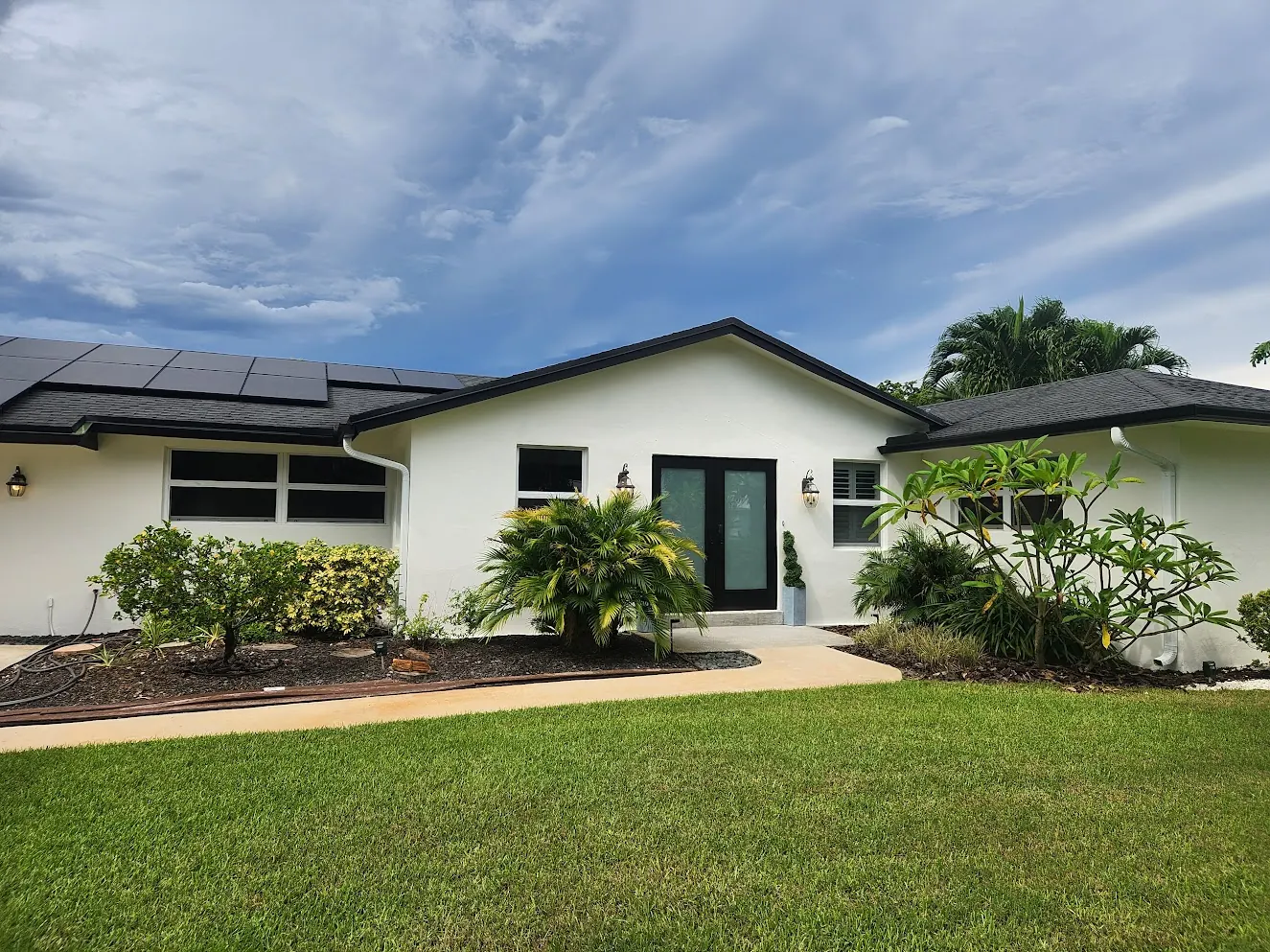 Single-story white home with a dark roof and black-framed windows after an exterior repaint
