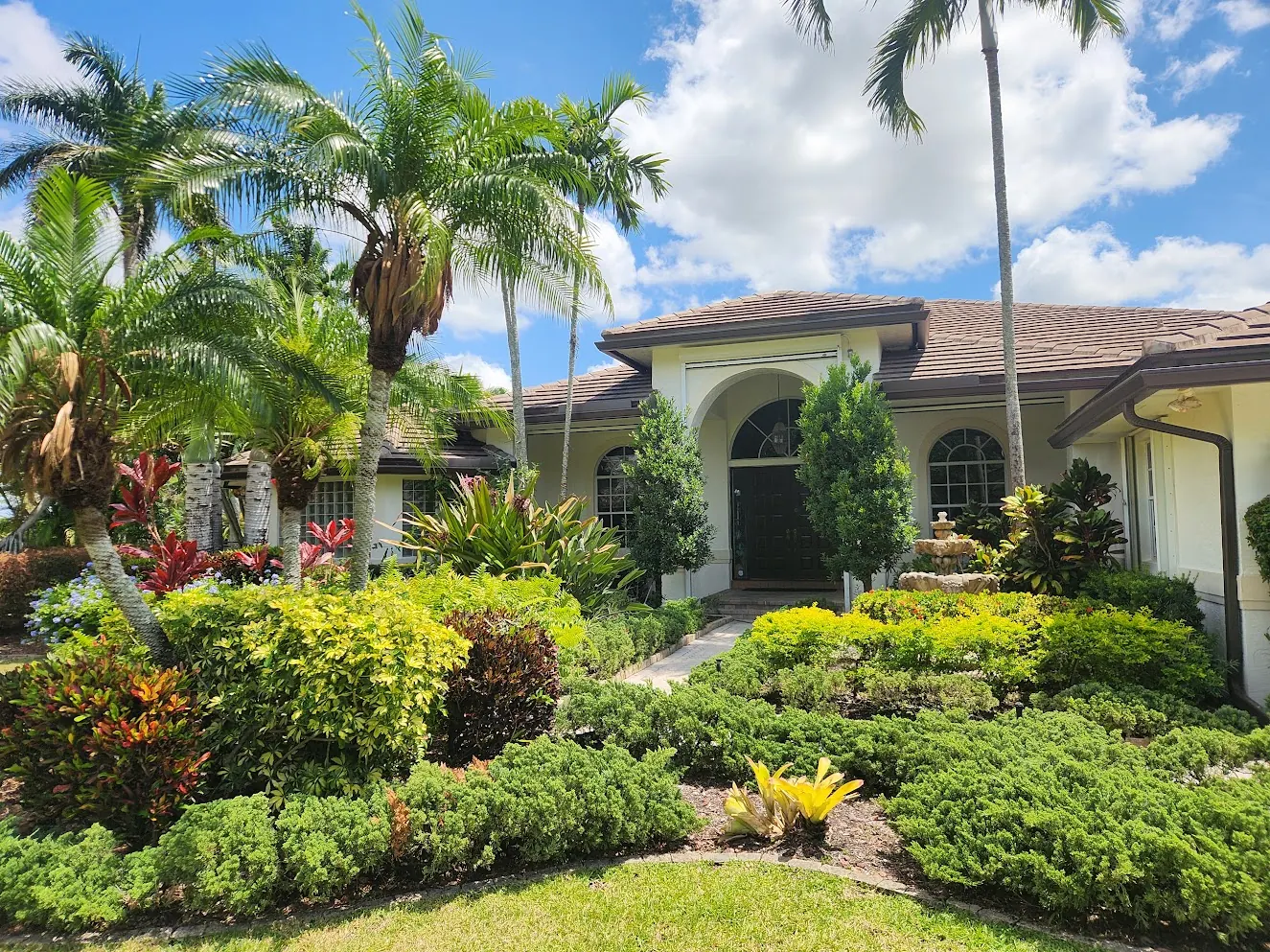 Home with an arched entry surrounded by tropical landscaping after an exterior repaint