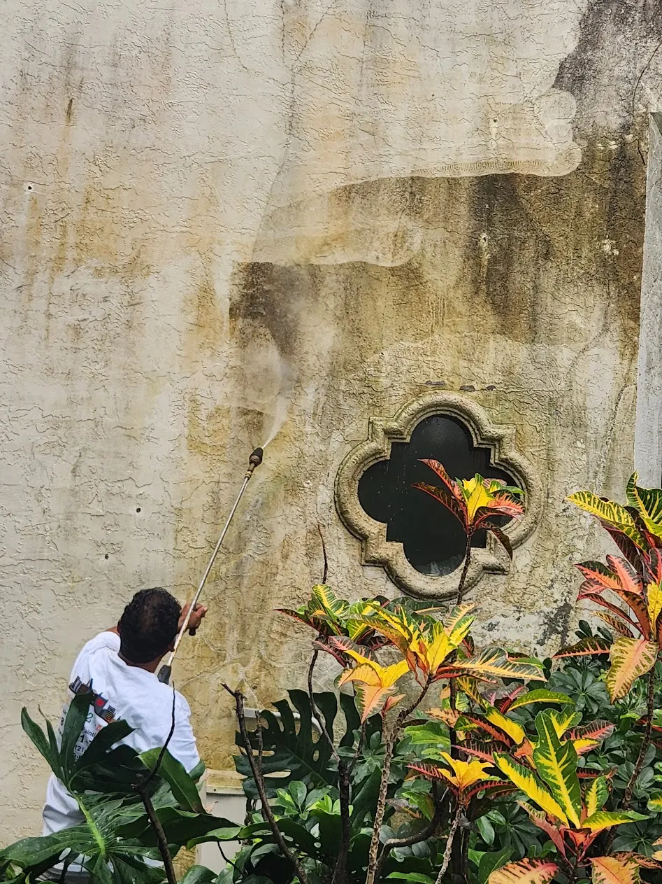 Pressure-cleaning the stained stucco wall around a quatrefoil window